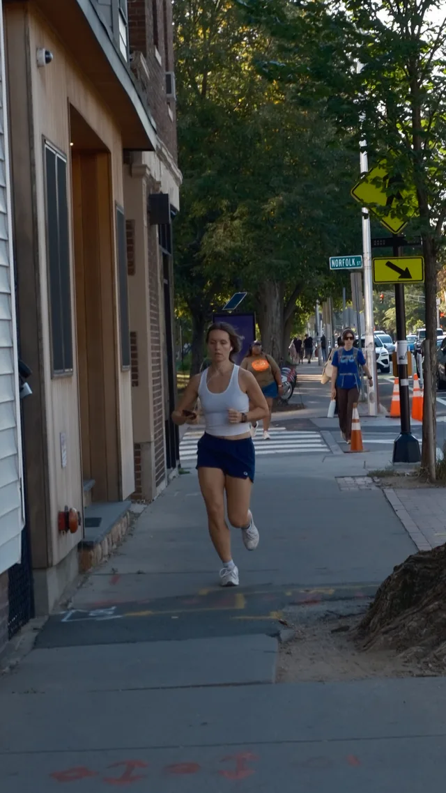 A runner approaches along a narrow tree-lined sidewalk.