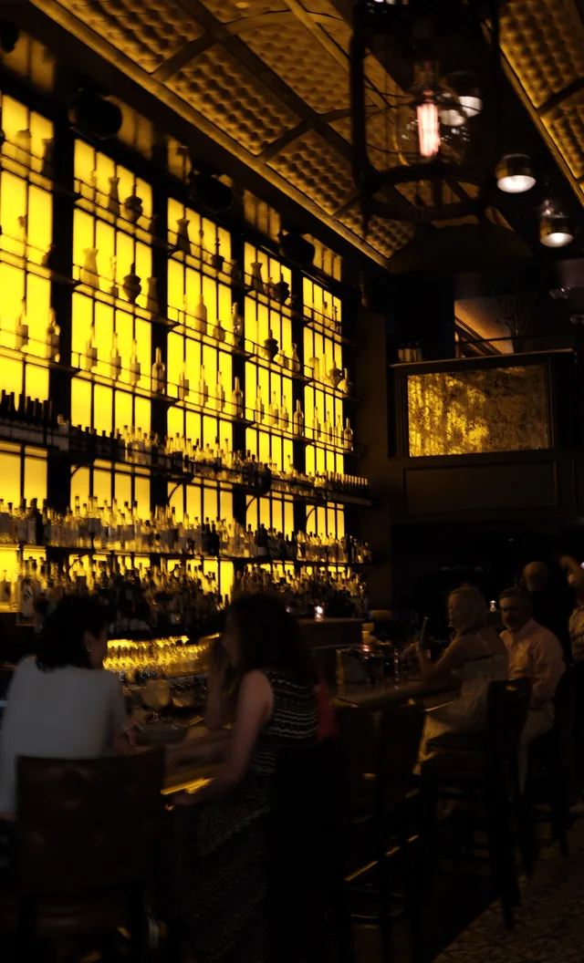 Backlit bottles form a tall amber wall behind a bar.