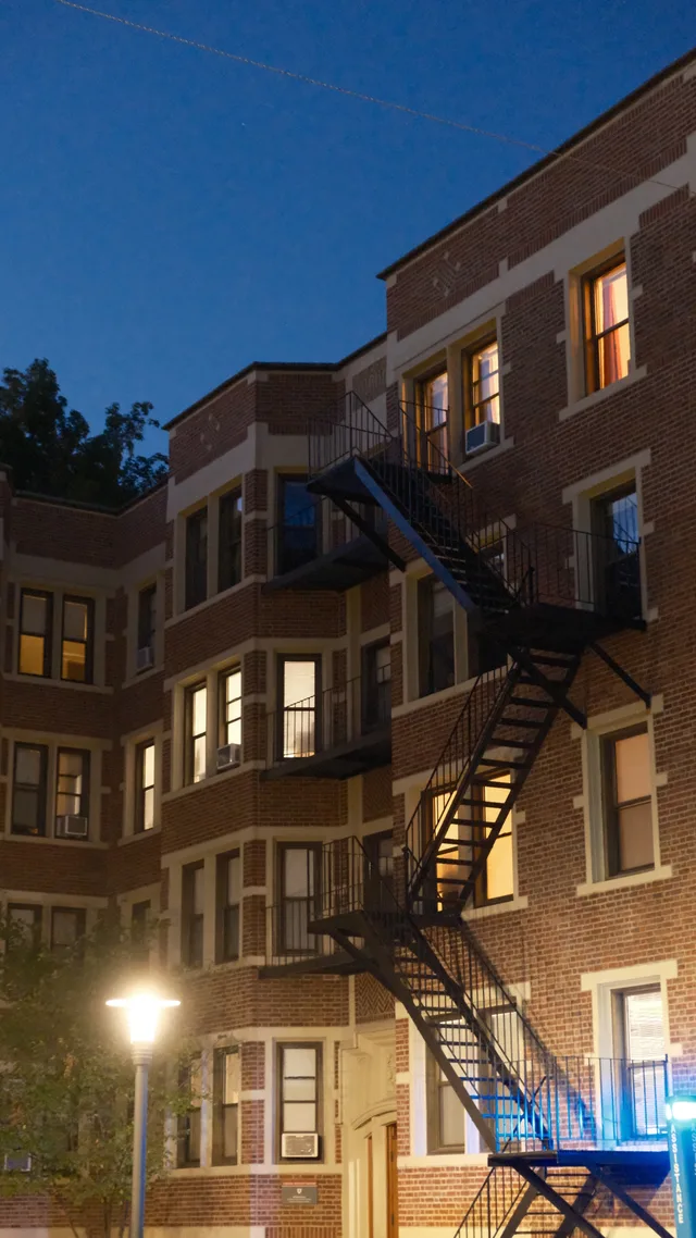 Lit apartment windows punctuate a brick facade beneath blue evening sky.